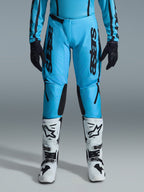 Alpinestars 2026 Stella Fluid Apex-byxor för dam, motocrossbyxor, klar cyan och svart, vertikal svart logotyp på låren, svarta förstärkta paneler på knänas insida, visas med vita och svarta motocross-stövlar och svarta handskar, professionell offroad-utrustning för damer