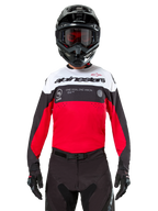 Alpinestars Pro-Dura Jersey, motocrosströja, svart, klarröd och vit, bärs med svart hjälm och goggles, sportig design med framträdande Alpinestars-logotyp och laserperforeringar, högpresterande enduro- och offroad-racingutrustning