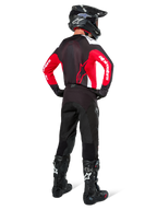 Motocrossförare sedd bakifrån klädd i Alpinestars Pro-Dura-tröja i svart, rött och vitt, matchad med svarta motocrossbyxor, hjälm och stövlar, visar ryggdesignen och ärmlogotyperna, koordinerad utrustning för terrängkörning.