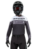 Motocrossförare som bär Alpinestars Pro-Dura Jersey i Black Magnet White, långärmad funktionströja med vita och grå färgblock, svart hjälm och goggles, 'alpinestars'-branding och slogan 'ONE GOAL ONE VISION', offroad-racingkläder
