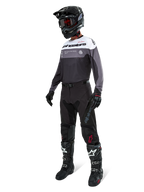 Alpinestars Pro-Dura-tröja i Black Magnet White, bärs av en motocrossförare i komplett utrustning inklusive svarta byxor, svart hjälm med goggles och svartvita stövlar. Tröjan har en teknisk färgblocksdesign med vita, grå och svarta paneler, konstruerad för enduro- och offroad-prestanda.
