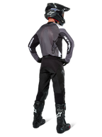 Motocrossförare iklädd Alpinestars Pro-Dura-tröja i Black Magnet White, vy bakifrån som visar grå ryggpanel i mesh och svarta ärmar med vit Alpinestars-logotyp, matchad med svarta byxor, svart hjälm och svartvita stövlar, professionell racingutrustning för enduro