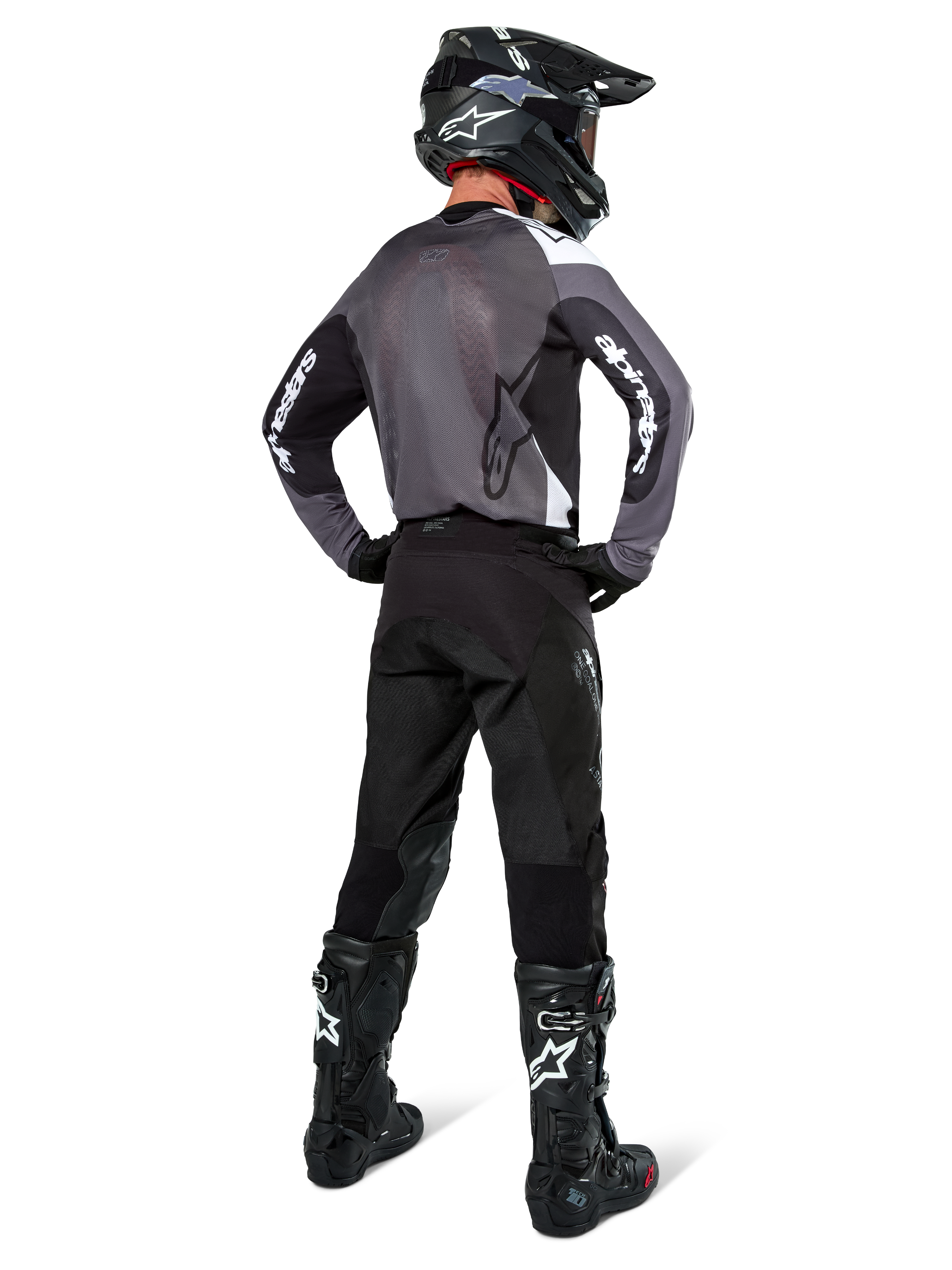 Motocrossförare iklädd Alpinestars Pro-Dura-tröja i Black Magnet White, vy bakifrån som visar grå ryggpanel i mesh och svarta ärmar med vit Alpinestars-logotyp, matchad med svarta byxor, svart hjälm och svartvita stövlar, professionell racingutrustning för enduro