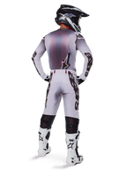 Motocross rider viewed from the back wearing the 2025 Supertech Maker Gear Set in White, featuring a grey and white jersey with black Alpinestars branding, matching motocross pants, white and black boots, and a black helmet, coordinated off-road racing kit