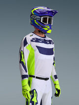 Motocrossförare iklädd Alpinestars 2026 Racer Air Riway-tröja, ljusgrå med neongula och blå detaljer, matchad med en blå och gul hjälm och neongula handskar, med ventilerande mesh-konstruktion och professionell racingstil för terrängprestanda.