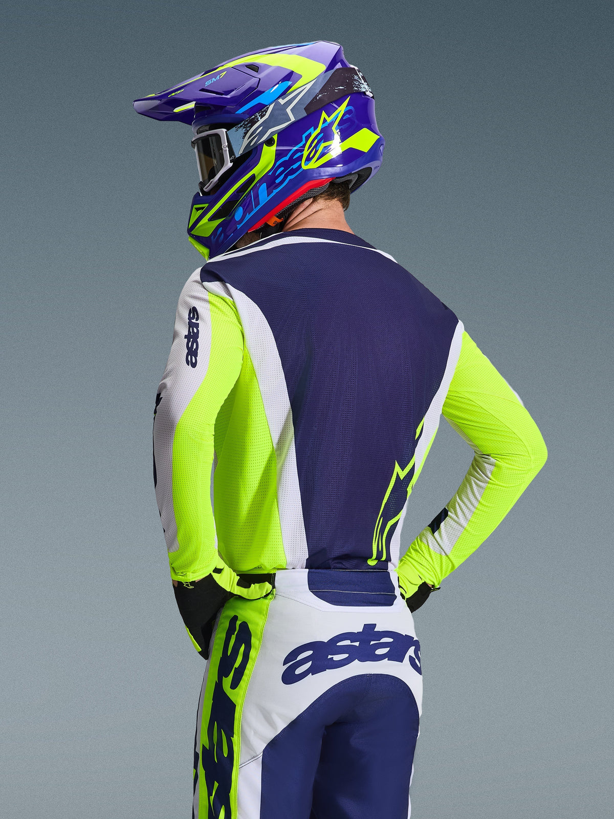 Alpinestars 2026 Racer Air Riway-tröja, motocrosströja, ljusgrå, neongul och blå, ryggvy av förare med matchande byxor och hjälm, atletisk tävlingspassform med ventilerande meshpaneler för terrängkörning