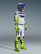 Motocross rider wearing complete racing gear, Light Gray jersey with Yellow Fluo and Blue accents, matching white and yellow pants, bright yellow boots and gloves, purple and yellow helmet with dark goggles, coordinated outfit for off-road racing