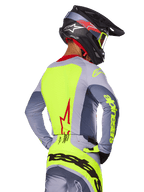 Alpinestars 2025 Techstar Melt-tröja, Bright Red Gray, vy bakifrån av motocrossförare i grå och neongul racingutrustning, röd stjärnlogotyp på ryggen, matchande svart och röd hjälm, högpresterande terrängkläder
