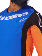Alpinestars 2025 Techstar Melt-tröja, motocrosströja, blå och orange med svarta paneler, vit Alpinestars-logotyp och synliga laserskurna perforeringar på bröstet, buren av en förare i svart hjälm