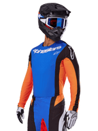 Alpinestars 2025 Techstar Melt utrustningsset, motocrossförare i blå tröja med orangea ärmar och svarta sidopaneler, matchande blå och svarta byxor, svart hjälm med blå goggles, vita och svarta handskar, atletiska motocrosskläder med race-passform