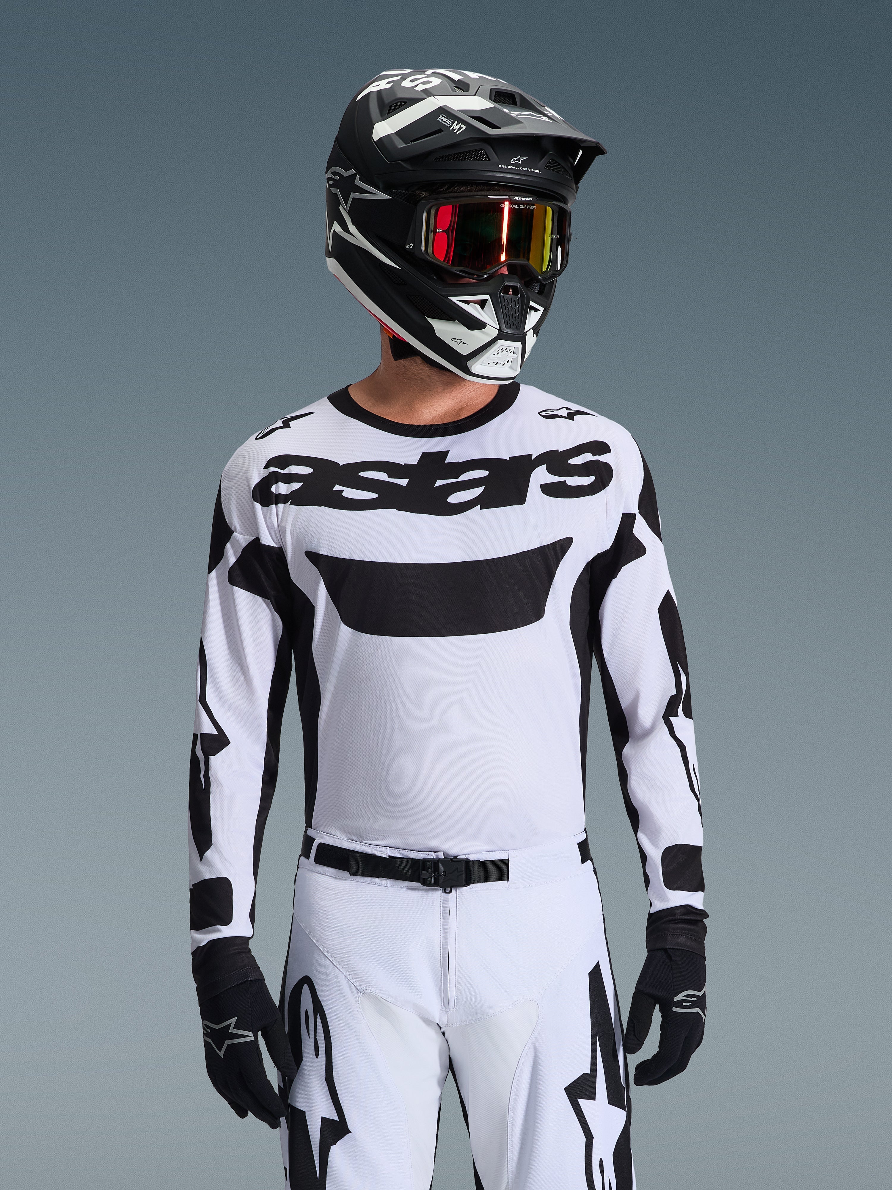 Motocrossförare i Alpinestars 2026 Racer Riway-tröja i vitt och svart, med 'astars'-logotyp på bröstet, matchande vita och svarta byxor, svart hjälm med goggles och svarta handskar, koordinerat ställ för terrängkörning