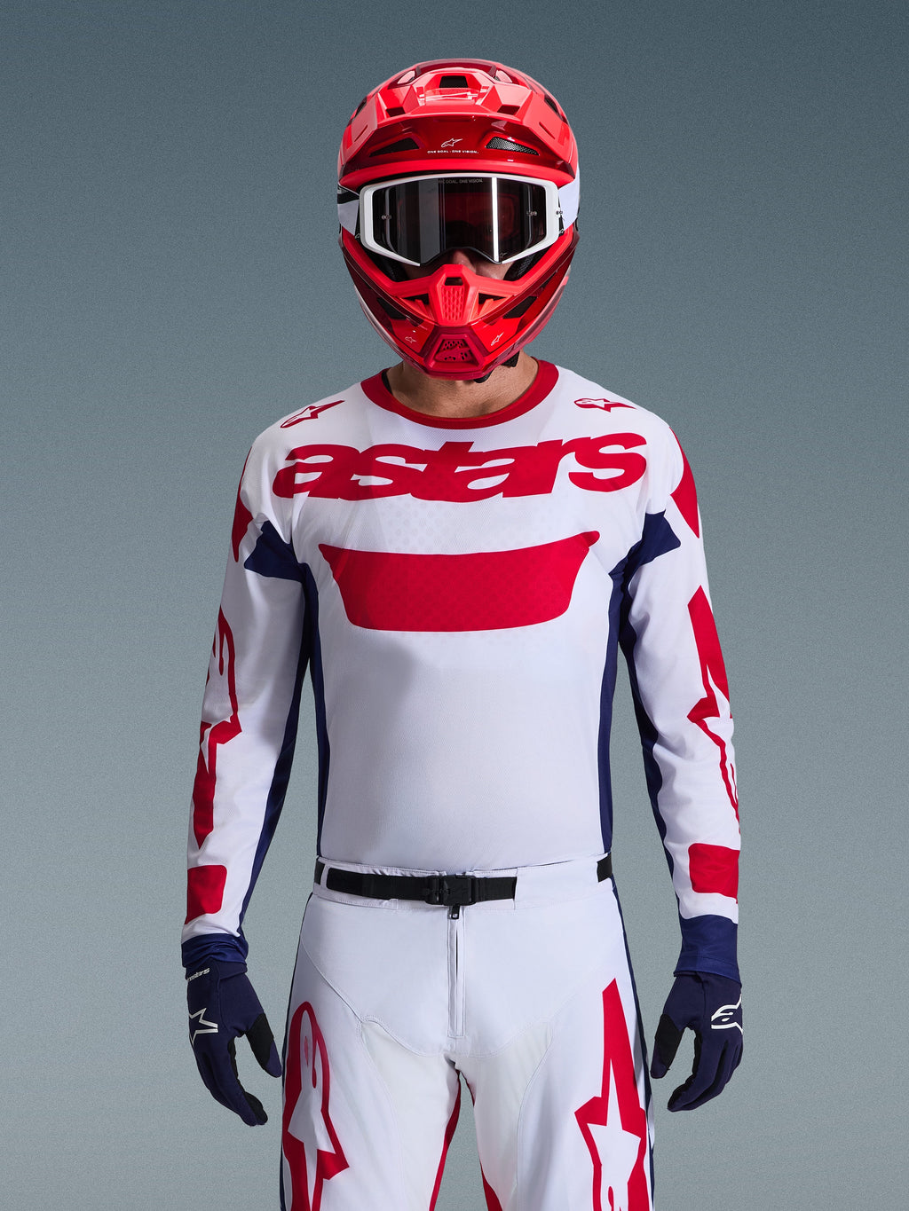Alpinestars 2026 Racer Riway-utrustningsset, motocrossförare i vit tröja med röd logotyp och marinblå detaljer, matchande vita byxor med röd grafik, röd hjälm med vita goggles, marinblå handskar, koordinerad professionell racingoutfit för terrängkörning.