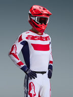 Motocrossförare som bär Alpinestars 2026 Racer Riway-tröja i vitt, blått och rött, matchande offroad-byxor, klarröd hjälm med vita goggles och marinblå handskar, koordinerat högpresterande utrustningsset för motocross