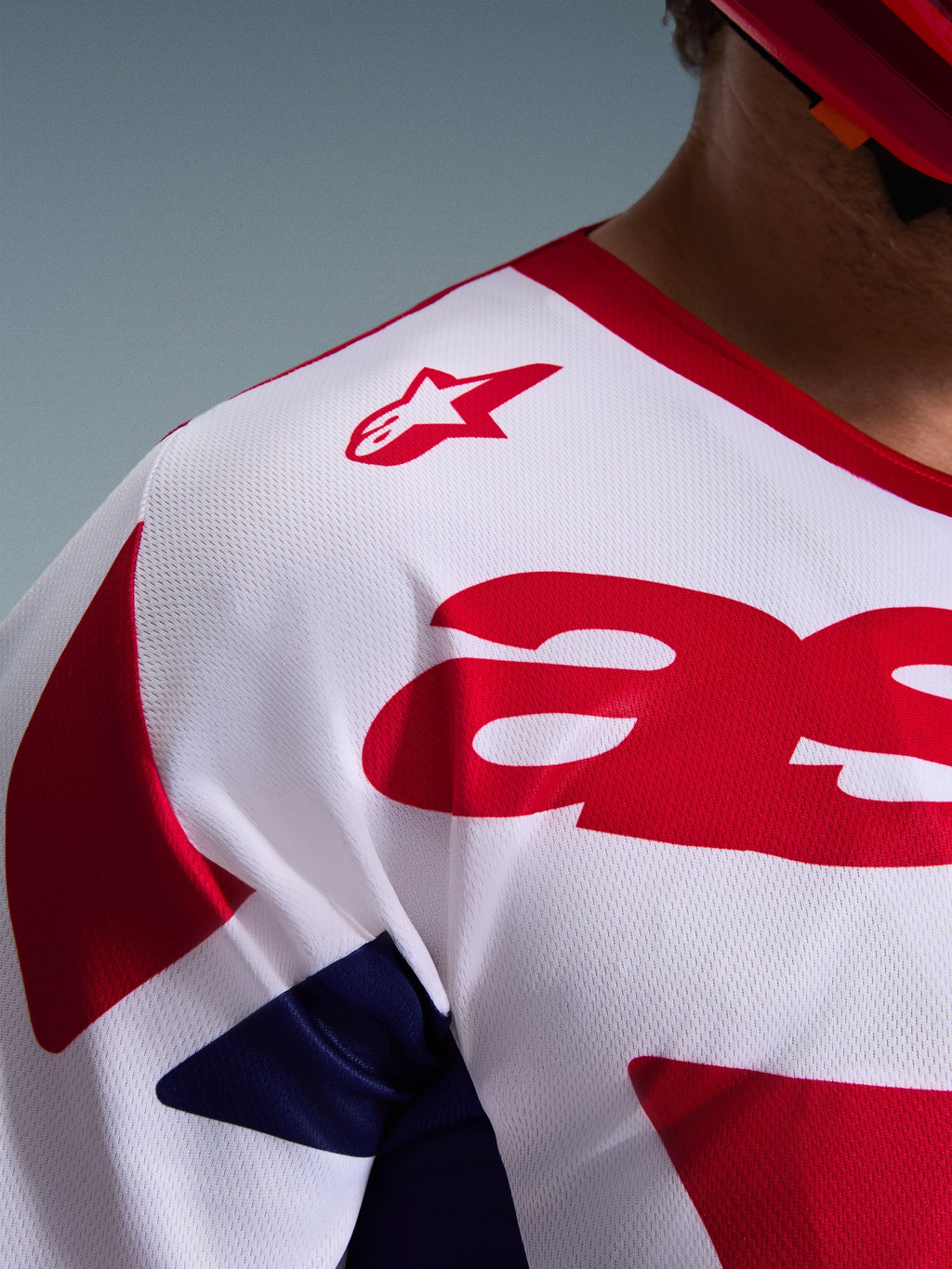 Närbild på Alpinestars 2026 Racer Riway-tröja, motocrosströja i vitt, blått och rött, med ventilerande fukttransporterande mesh-struktur, röd stjärnlogotyp på axeln och kraftfull röd grafik på bröstet
