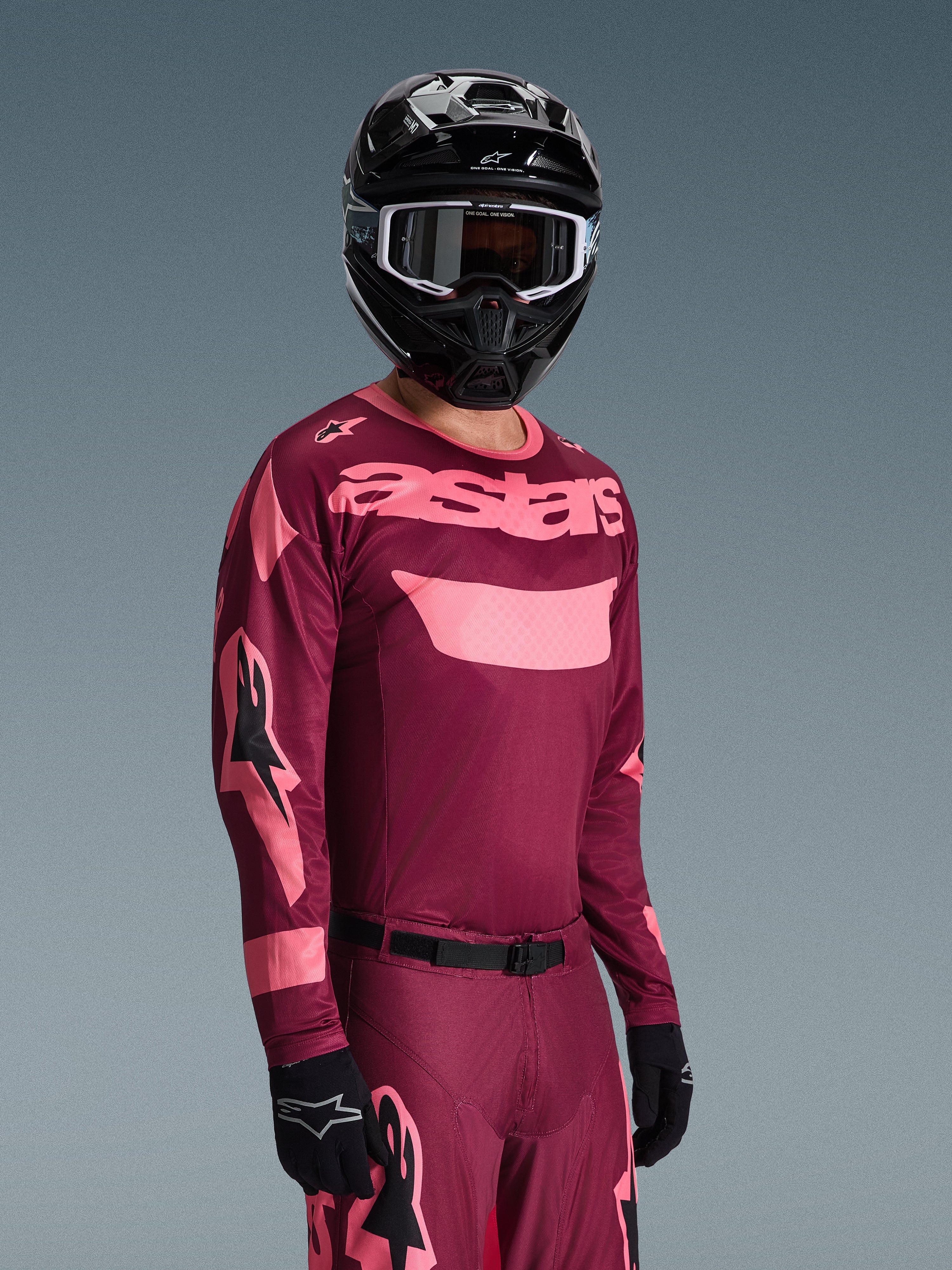 Motocross rider wearing Alpinestars 2026 Racer Riway Gear Set, Burgundy and Pink jersey with bold 'astars' branding, matching pants with pink accents, black helmet and gloves, professional racing outfit for off-road motocross