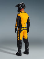 Motocrossförare bakifrån klädd i Alpinestars 2026 Racer Riway-ställ, gul och svart tröja med matchande byxor, svart hjälm, svarta handskar och svarta stövlar med vita detaljer, koordinerad outfit för professionell terrängkörning.