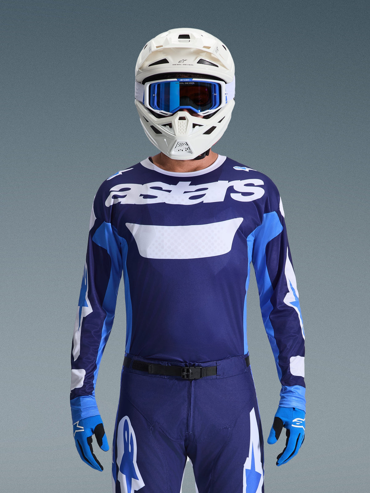 Motocross rider wearing Alpinestars 2026 Racer Riway Jersey, UCLA Blue and White with white 'astars' logo on chest, white helmet with blue goggles, matching motocross pants and blue gloves, coordinated off-road racing gear