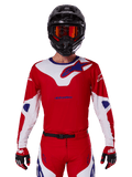 Alpinestars 2025 Racer Veil tröja, motocross-racingtröja, röd, vit och blå, långärmad, bärs med svart hjälm och orangefärgade goggles, matchande röda handskar och byxor, strömlinjeformad prestandadesign för terrängkörning