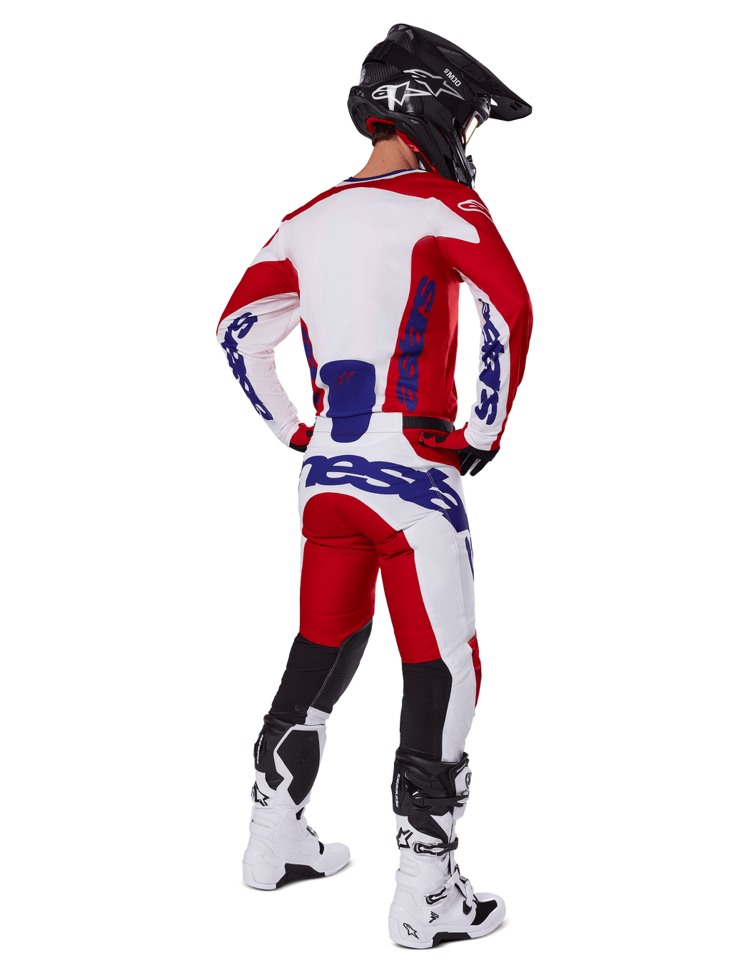 Motocrossförare sedd bakifrån bär Alpinestars 2025 Racer Veil tröja och byxor i rött och vitt, med blå logotyper, svart hjälm och vita stövlar, komplett utrustningsset för terrängkörning