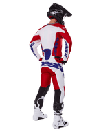 Motocrossförare sedd bakifrån bär Alpinestars 2025 Racer Veil tröja och byxor i rött och vitt, med blå logotyper, svart hjälm och vita stövlar, komplett utrustningsset för terrängkörning