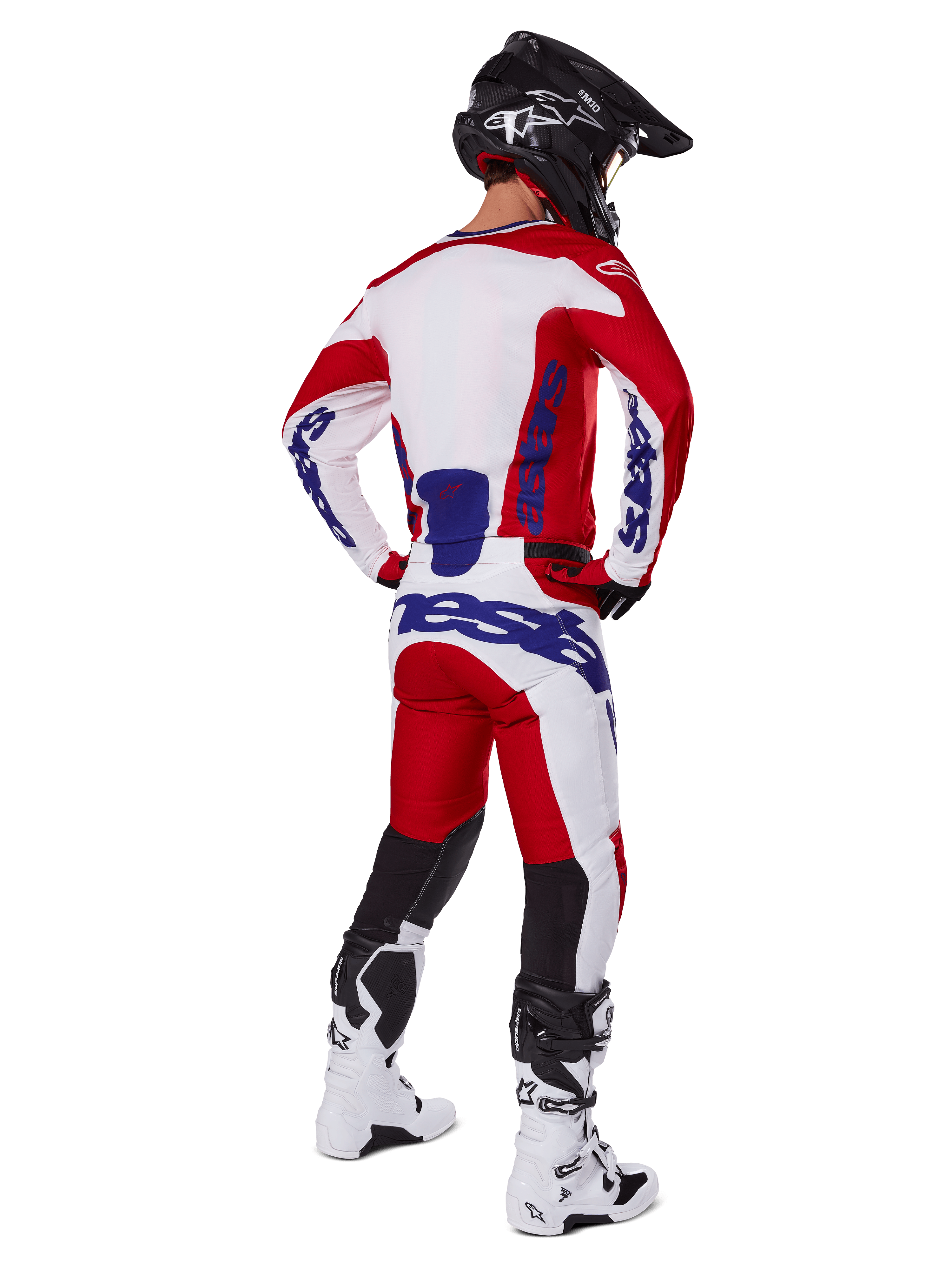 Motocrossförare sedd bakifrån bär Alpinestars 2025 Racer Veil tröja och byxor i rött och vitt, med blå logotyper, svart hjälm och vita stövlar, komplett utrustningsset för terrängkörning