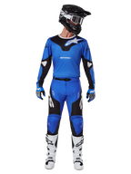 Motocross rider wearing the Alpinestars 2025 Racer Veil Gear Set, blue and black jersey with matching pants, black helmet with white goggles, white and black boots, coordinated racing outfit for off-road motocross.