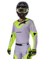Motocross rider wearing Alpinestars 2025 Racer Veil Gear Set in Gray and fluo green, light gray jersey and pants with bold neon yellow-green panels and black Alpinestars logos, coordinated with matching gloves and a black helmet with neon green goggles, professional off-road racing apparel.