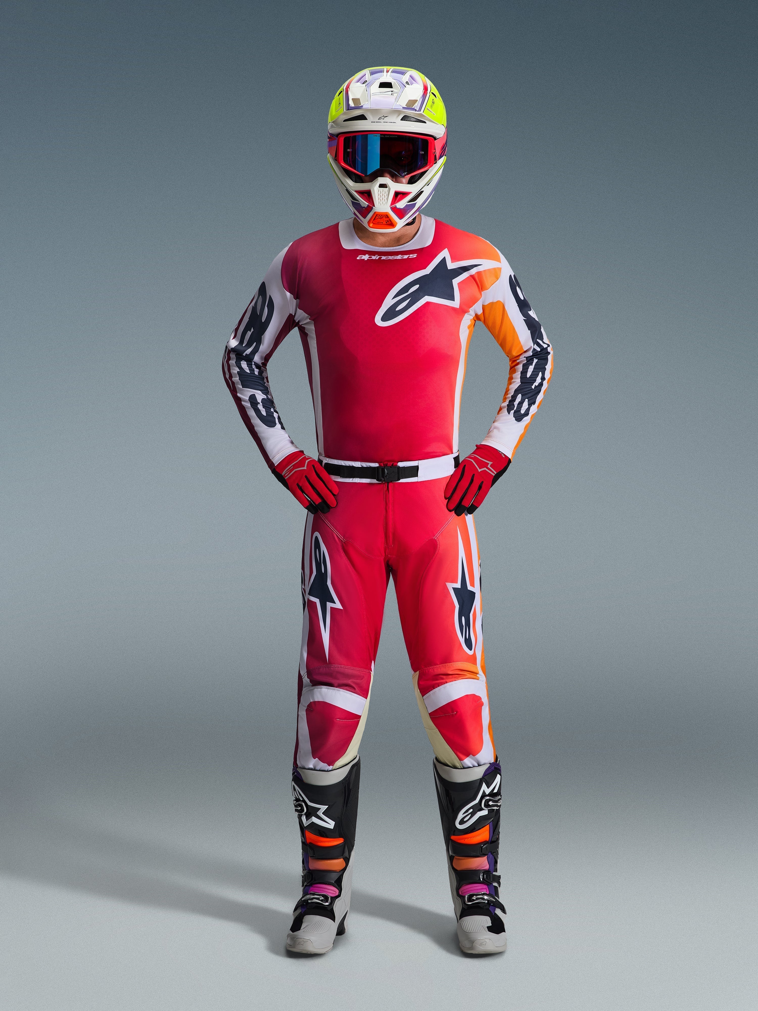 Motocrossförare bär Alpinestars 2026 Racer Portl-tröja i rött med vita och orange grafiska detaljer, matchande motocrossbyxor, röda handskar, en färgglad racinghjälm med goggles och svarta och vita tekniska stövlar, komplett utrustningsset för terrängkörning.
