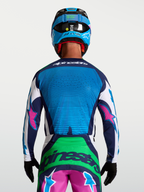 Alpinestars Techstar Maven tröja för terrängkörning, blå och grön med rosa detaljer, bärs av en modell bakifrån med hjälm och handskar, laserskuren ventilation för optimalt luftflöde.