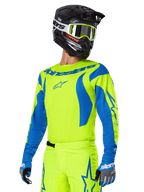 Alpinestars 2025 Fluid Haul-utrustningsset, motocrosströja och byxor, klar gul och blå, bärs med en svart hjälm och goggles med gula bågar, har vågliknande blå mönster på ärmarna och blå stjärnlogotyper på byxorna, matchande outfit för terrängkörning