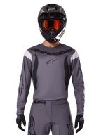 Motocross rider wearing the 2025 Fluid Haul Jersey and Gear Set, Gray with black and white accents, featuring long sleeves and bold branding, black helmet with orange goggles, and black gloves, coordinated outfit for off-road racing