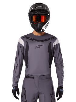 Motocross rider wearing the 2025 Fluid Haul Jersey and Gear Set, Gray with black and white accents, featuring long sleeves and bold branding, black helmet with orange goggles, and black gloves, coordinated outfit for off-road racing