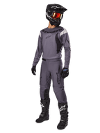 Motocross rider wearing Alpinestars 2025 Fluid Haul Gear Set in Gray, including gray jersey and pants with black accents, black helmet with reddish goggles, black gloves, and black boots with white logos, complete off-road racing outfit