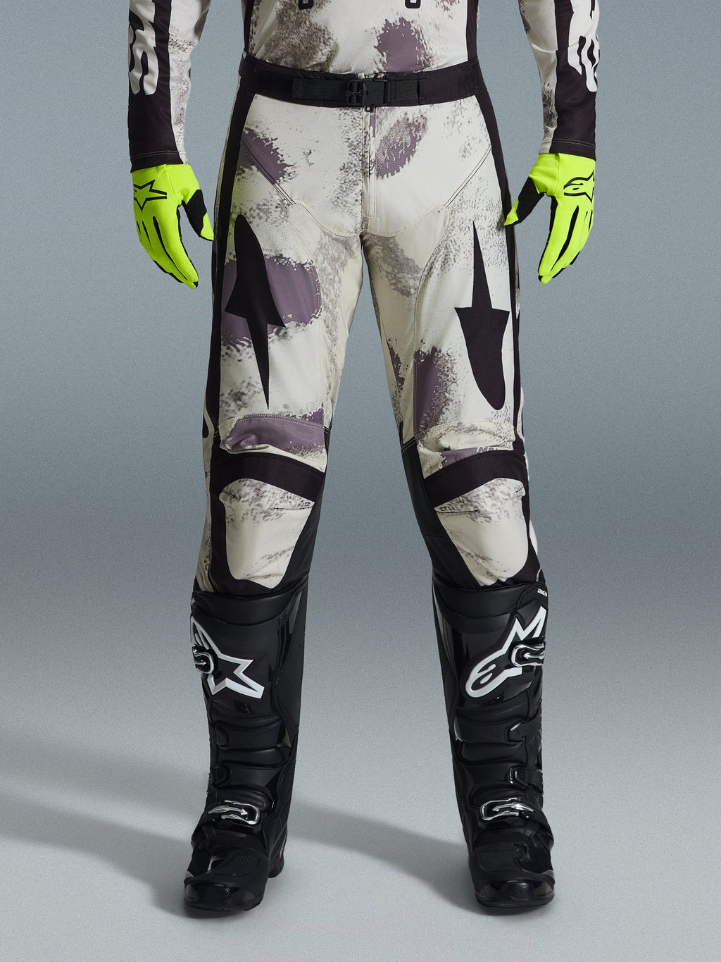 Alpinestars 2026 Racer Lahnd byxor, motocrossbyxor, Sand Camo-mönster med grå och lila abstrakt grafik, bärs med neongula handskar och svarta stövlar, svarta stjärnlogotyper på låren och ett svart midjebälte, hållbar racingutrustning för terrängkörning