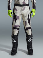 Alpinestars 2026 Racer Lahnd byxor, motocrossbyxor, Sand Camo-mönster med grå och lila abstrakt grafik, bärs med neongula handskar och svarta stövlar, svarta stjärnlogotyper på låren och ett svart midjebälte, hållbar racingutrustning för terrängkörning