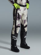Alpinestars 2026 Racer Lahnd byxor, motocrossbyxor, Sand Camo, bärs med neongula handskar och svarta motocross-stövlar, med ett abstrakt kamouflagemönster med svarta sidopaneler, ergonomisk offroad-design