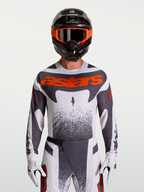 Alpinestars Techstar Swan tröja, motocrosströja för herrar i vit och grå med röd fluo, atletisk racingpassform och laserperforeringar för ventilation, visas på modell med matchande utrustning.