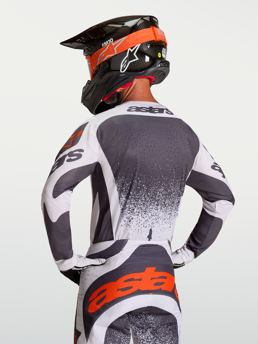 Alpinestars Techstar Swan tröja, motocrosströja i mörkgrått och vitt med röda detaljer, atletisk tävlingspassform visas bakifrån på förare med hjälm för terrängkörning.