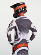 Alpinestars Techstar Swan tröja, motocrosströja i mörkgrått och vitt med röda detaljer, atletisk tävlingspassform visas bakifrån på förare med hjälm för terrängkörning.