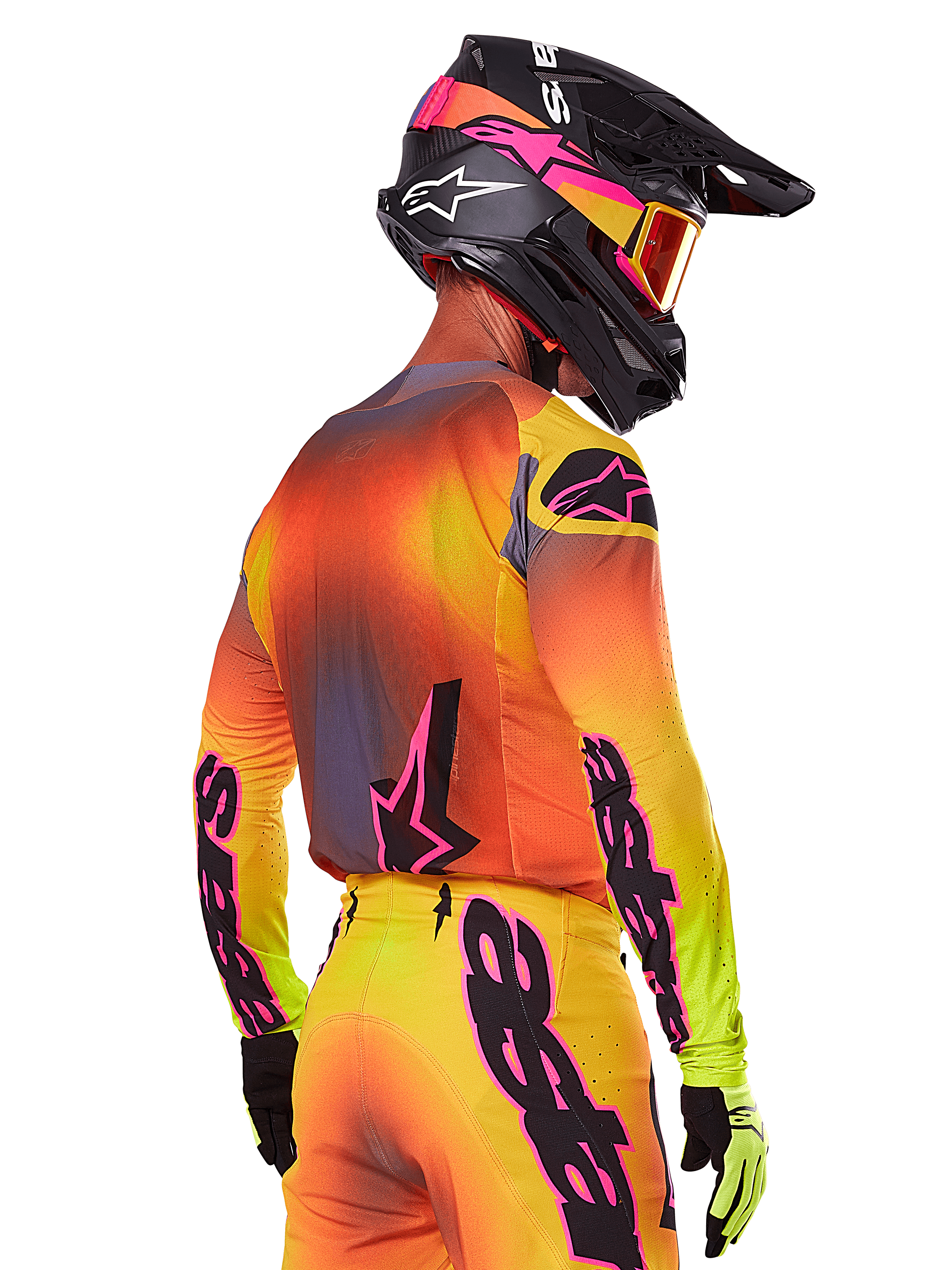 Motocrossförare sedd snett bakifrån iklädd Alpinestars 2025 Supertech Lipan Gear Set, med en färgtoning i gult, orange och rött med svarta och rosa logotyper, svart hjälm med rosa detaljer och orangea goggles, professionell utrustning för terrängkörning.