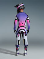 Motocrossförare sedd bakifrån iklädd Alpinestars 2026 Supertech AFD Vista utrustningsset, tröja och byxor med en livfull färggradient i vitt, lila och rosa med svarta detaljer, svart hjälm med lila goggles, matchande lila och vita stövlar, koordinerad professionell racingoutfit för terrängprestanda
