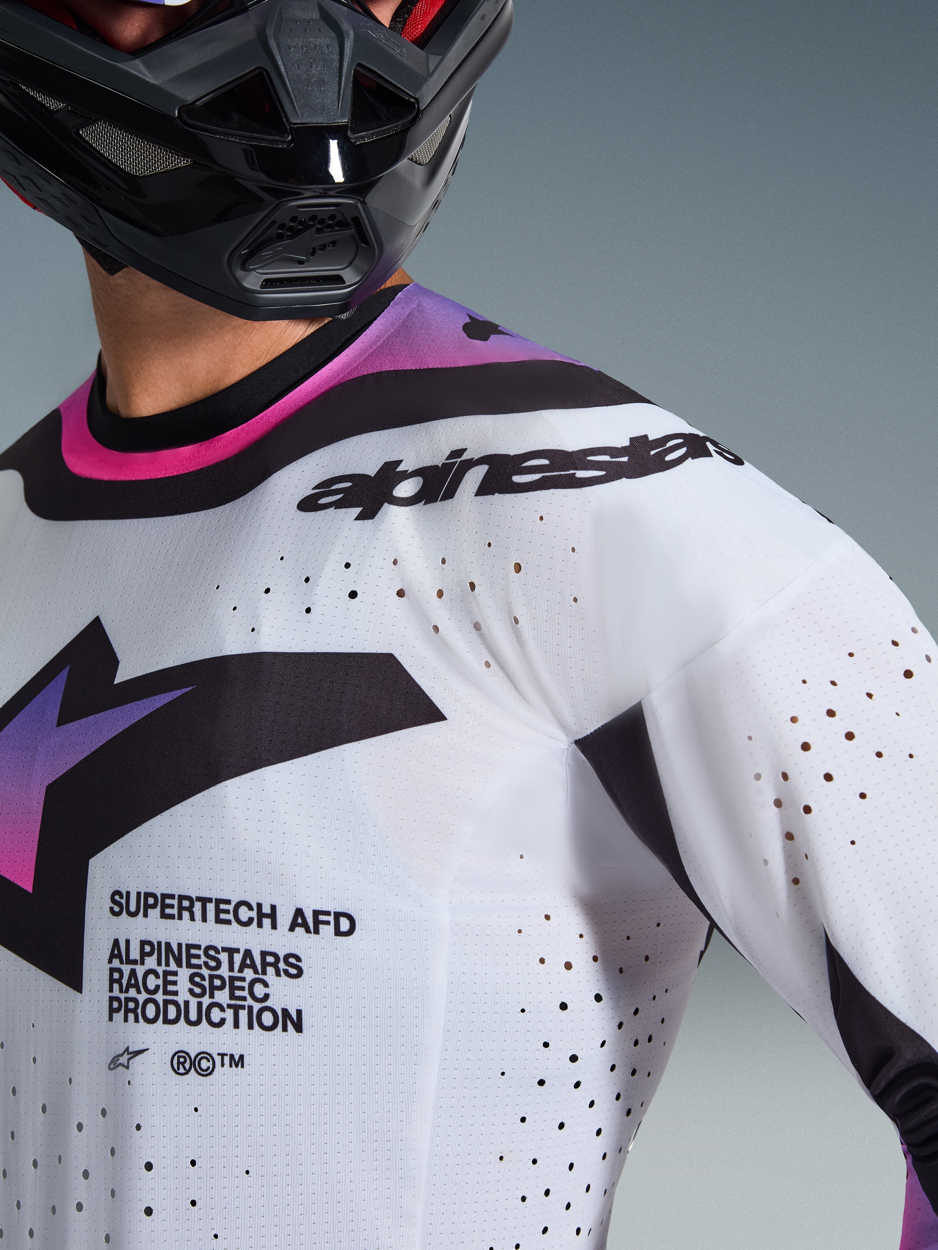 Närbild av en motocrossförare som bär 2026 Supertech AFD Vista Jersey i vit, lila och svart, med laserskurna perforeringar för ventilation, "SUPERTECH AFD"-text på bröstet och svart Alpinestars-branding på axeln, atletisk racingutrustning för terrängkörning.