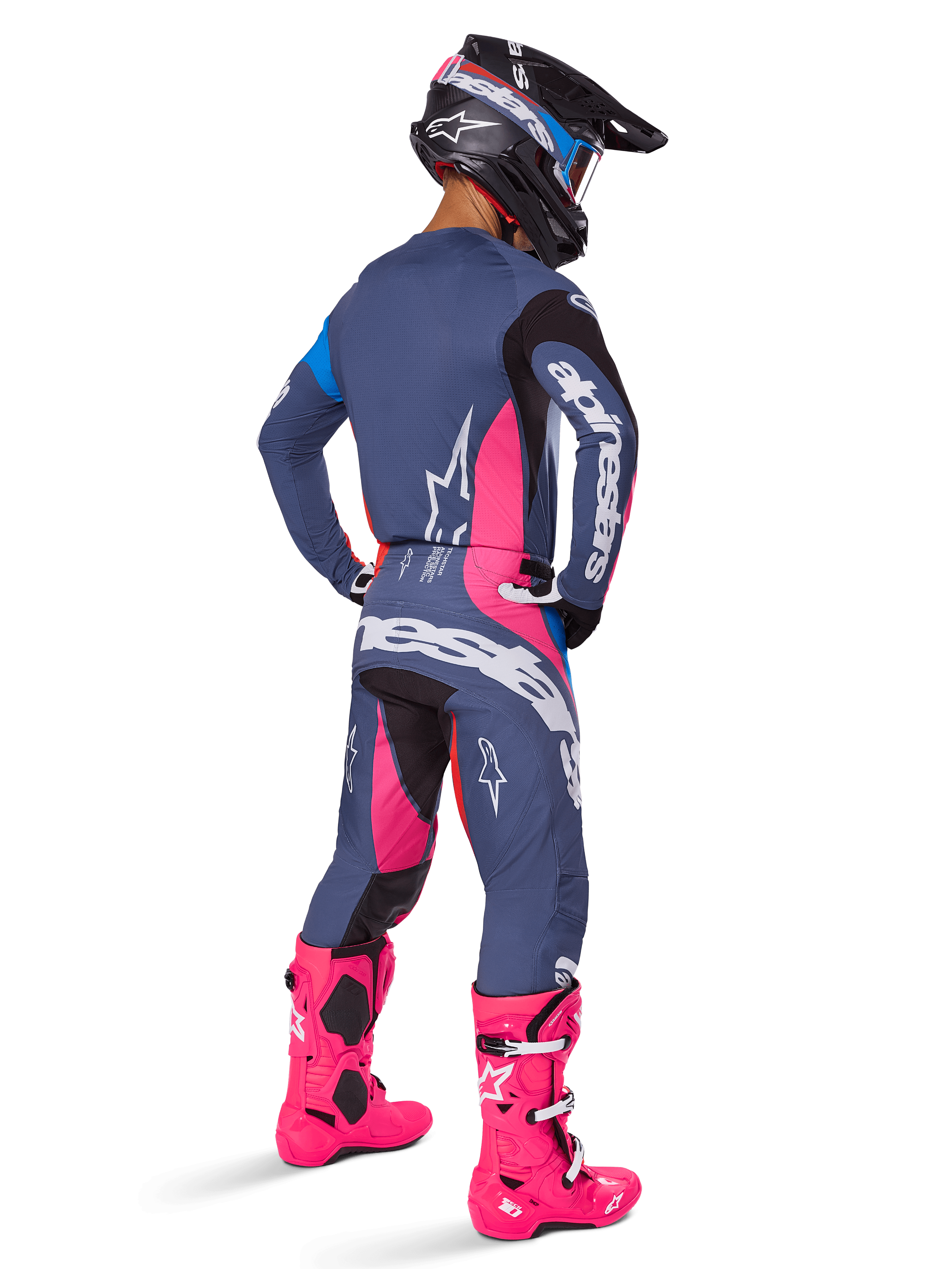 Motocrossförare sedd bakifrån, bär Alpinestars 2025 Techstar Dreem-utrustningsset, grått med livfulla rosa och vita detaljer, svart och vit hjälm och klarrosa stövlar, komplett tävlingsoutfit för motocrossprestanda.