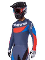 Alpinestars 2025 Techstar Dreem utrustningsset, motocrossförare i skiffergrå tröja och byxor med framträdande röd och blå grafik, 'astars'-logotyp på bröstet, matchat med en svart hjälm, röda goggles och vita racinghandskar