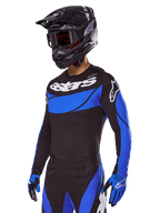 Motocrossförare i Alpinestars 2025 Techstar Dreem Gear Set, svart tröja med blå paneler i perforerad stil och vit logotyp, matchande svarta och blå byxor, svart racinghjälm och blå handskar, koordinerad förarutrustning för motocross.