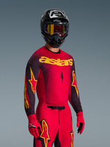 Motocrossförare i Alpinestars 2026 Supertech Scenz-tröja i rött och svart med gul 'astars'-logotyp, matchande röda byxor och handskar, svart hjälm med goggles, professionell racingutrustning för terrängmotocross