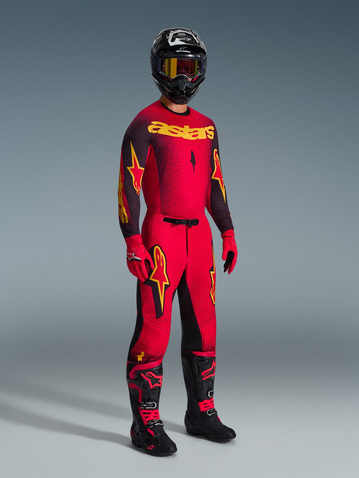 Motocross rider wearing the Alpinestars 2026 Supertech Scenz Jersey in Red Black Yellow, matching red pants with black and yellow accents, black helmet with goggles, red gloves, and black boots with red details, complete professional racing gear set.