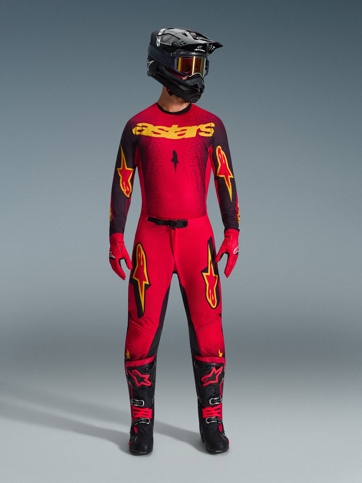 Alpinestars 2026 Supertech Scenz Gear Set, complete motocross racing outfit in red and black with yellow graphics, featuring a pro-level jersey and matching pants, worn with a black helmet, red gloves, and black racing boots, premium performance gear for off-road competition