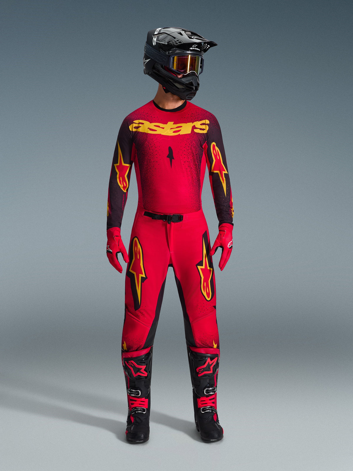 Motocross rider wearing the Alpinestars 2026 Supertech Scenz Jersey in Red Black Yellow, styled with matching pants, black helmet with goggles, red gloves, and black and red boots, professional racing gear set for off-road performance