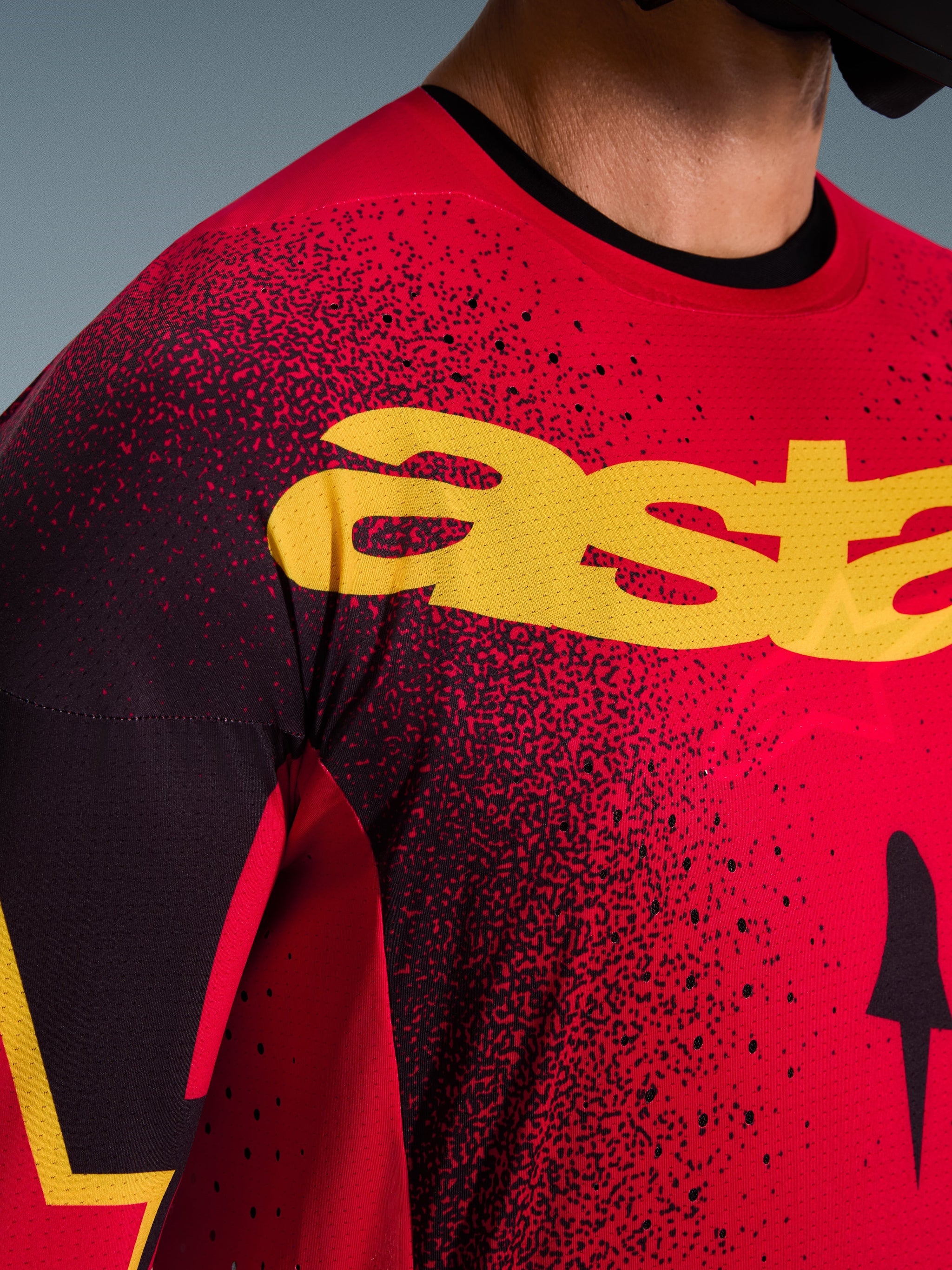 Alpinestars 2026 Supertech Scenz tröja, motocrosströja, röd, svart och gul, närbild på bröstpartiet med gul logotyp, svart spräckligt mönster och laserskurna perforeringar för ventilation.